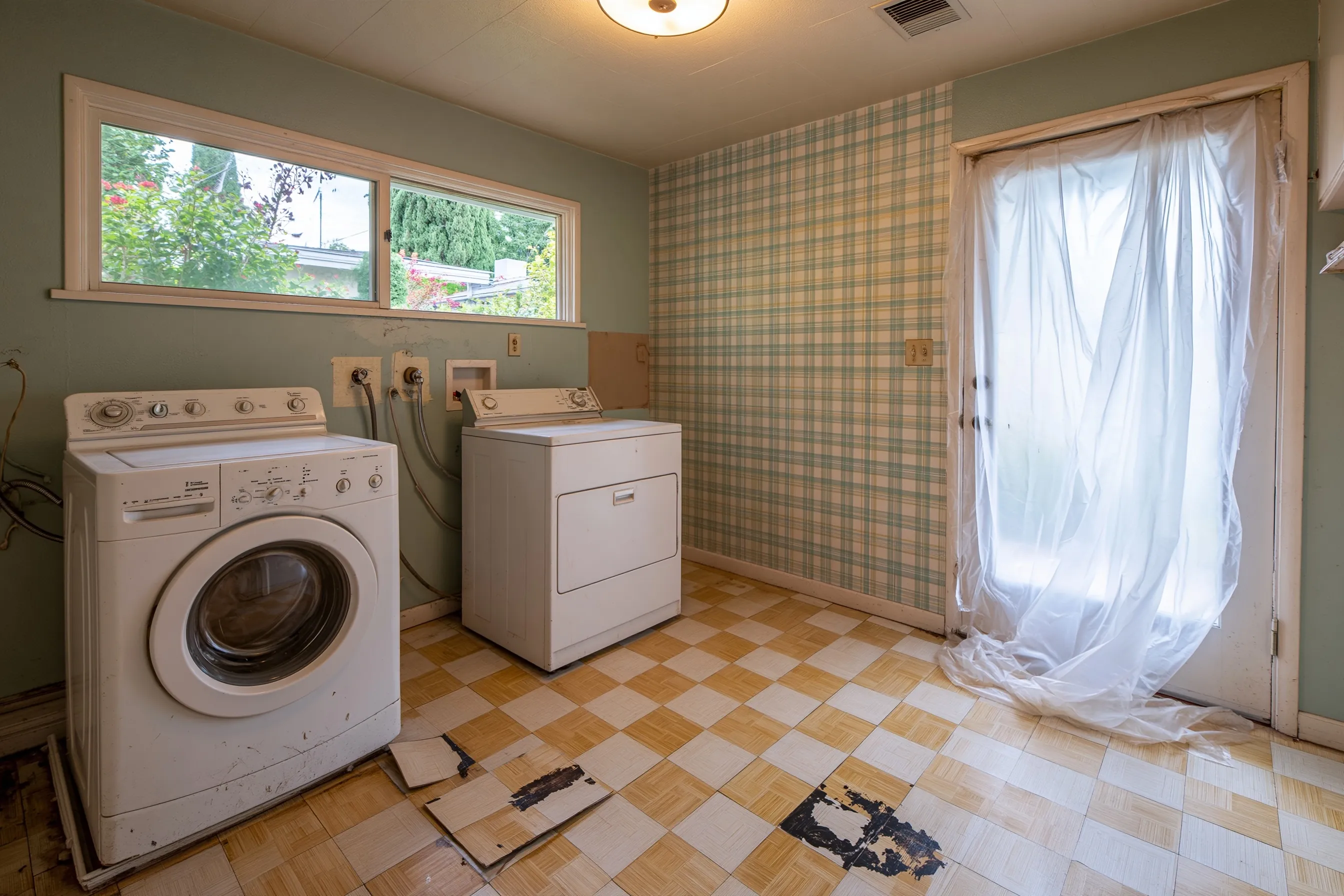 A 1960s laundry room with the machines moved out and 9-inch tiles lifted to show black adhesive