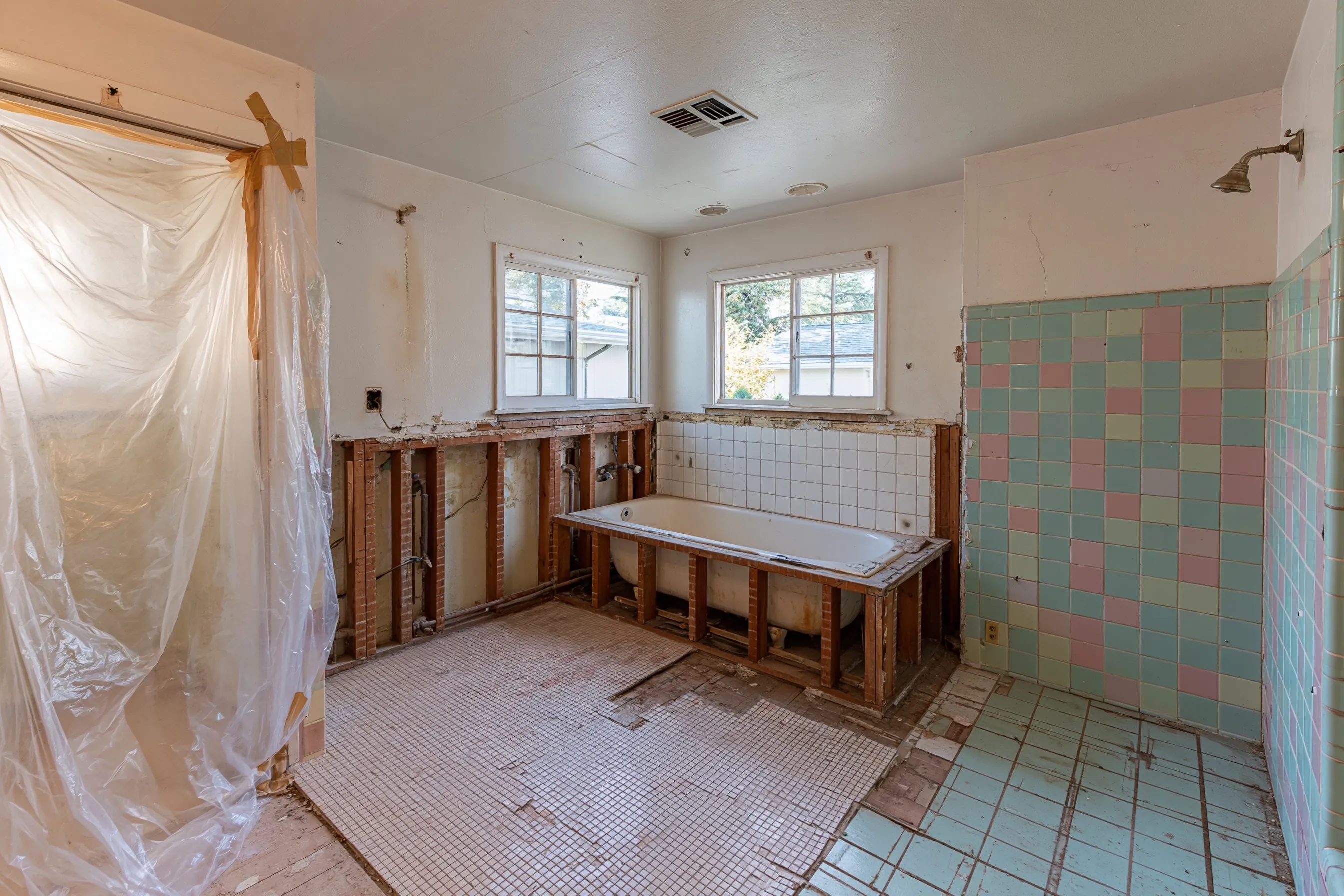 A 1950s bathroom mid-remodel with the tub wall cut away, floor tile lifted and plastic sheeting up